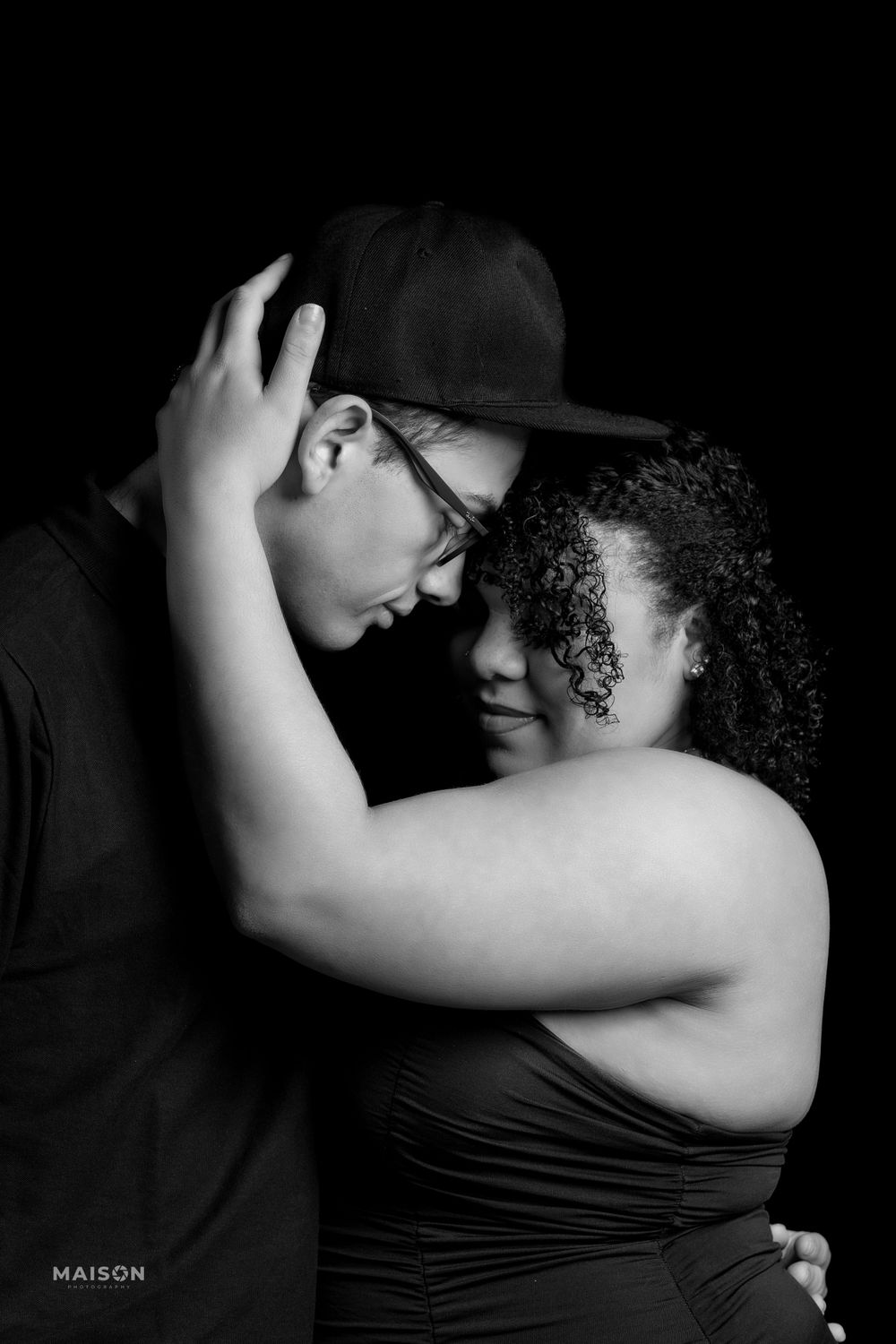 A black and white portrait of a romantic couple embracing intimately in an artistic studio photography session.
