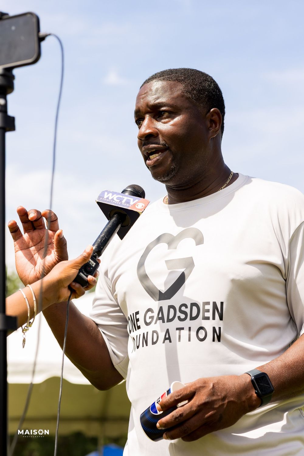 A person in a white Gadsden t-shirt gestures while speaking outdoors, shown in a sequence of photos.