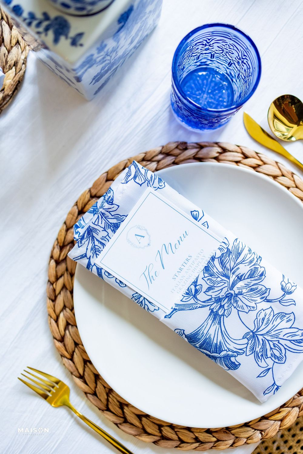 Close-up details of elegant blue and white place settings with woven placemats and gold cutlery for a formal dinner table.