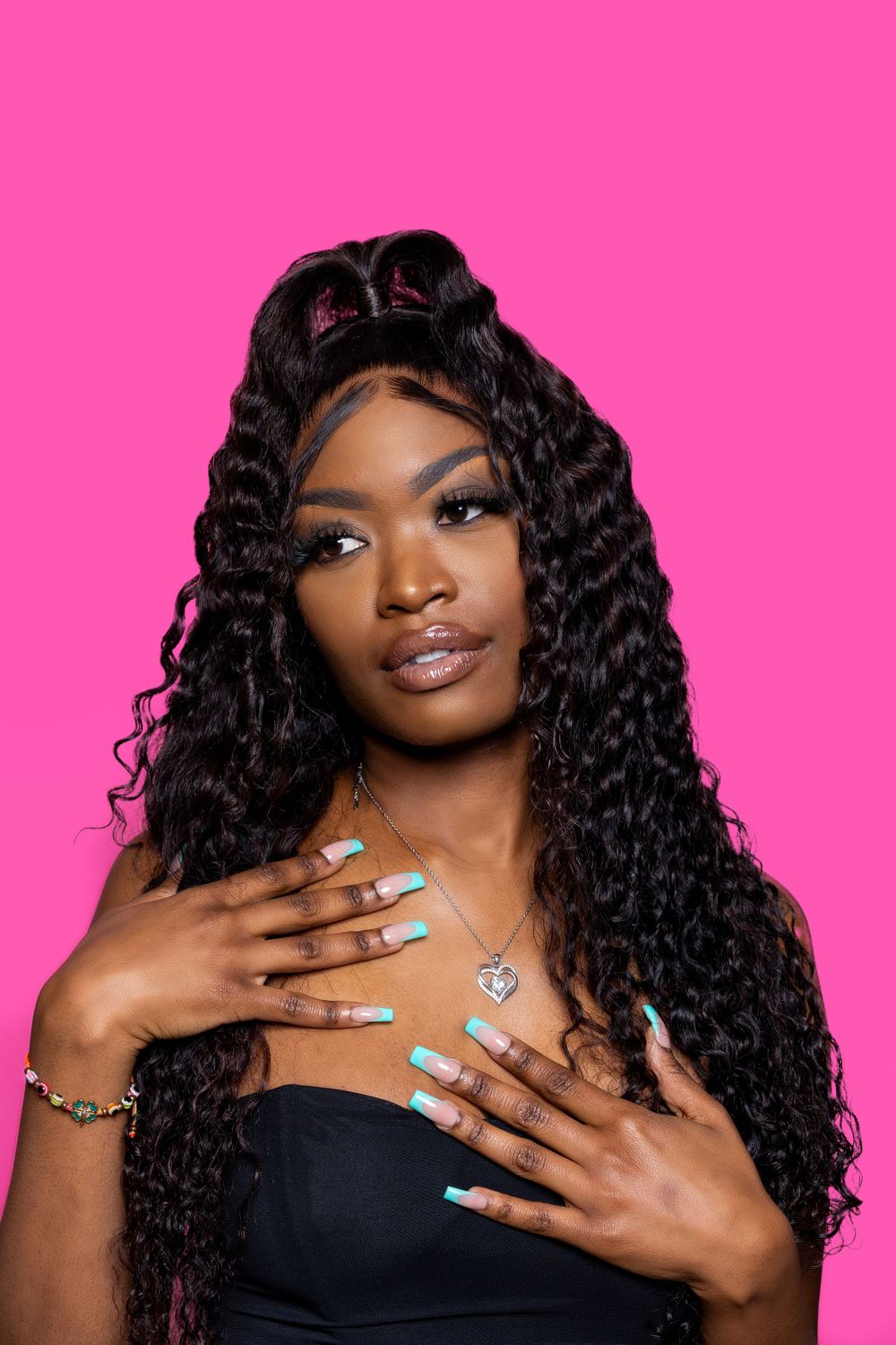 Portrait with long curly hair and blue nails against pink background.