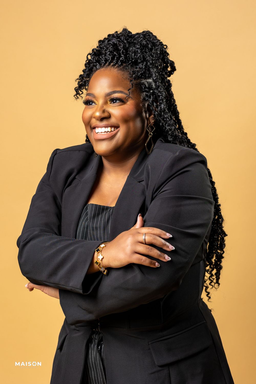 Professional portrait of someone in a black blazer smiling warmly against an orange background.