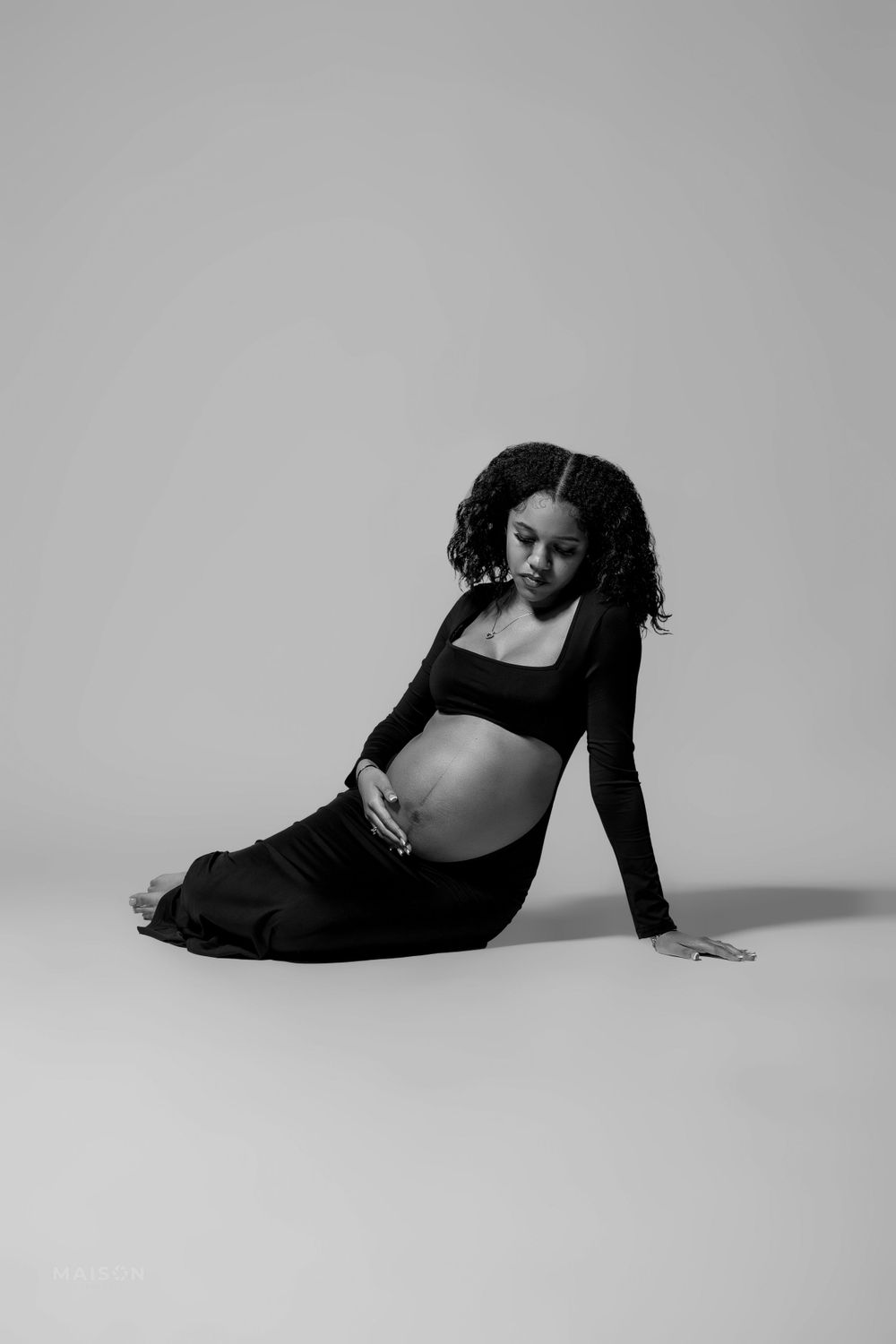 An artistic black and white maternity photo of an expectant mother in relaxed reclined pose.