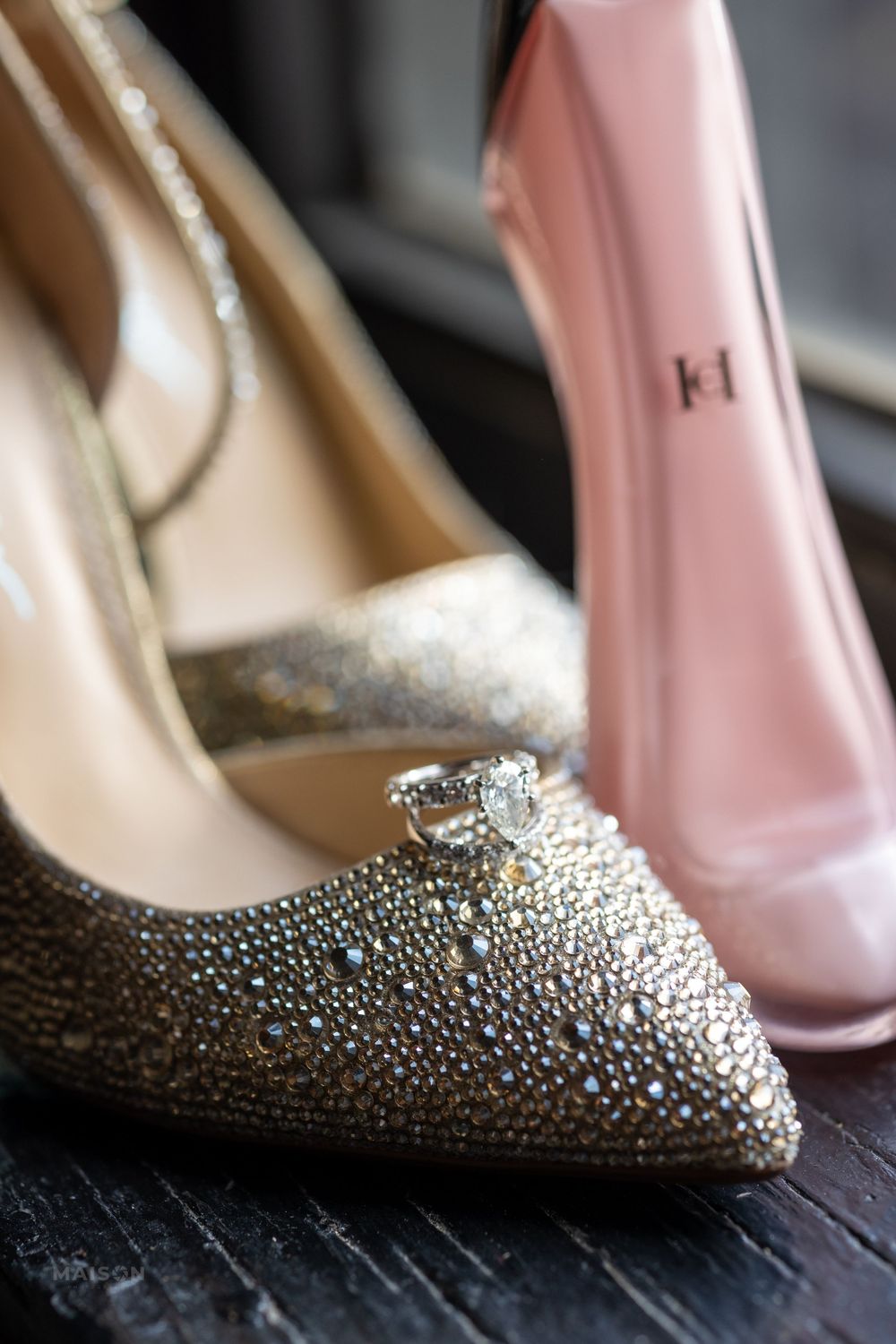 A close-up of a sparkly rhinestone-encrusted wedding heel next to a pink shoe on a dark surface.