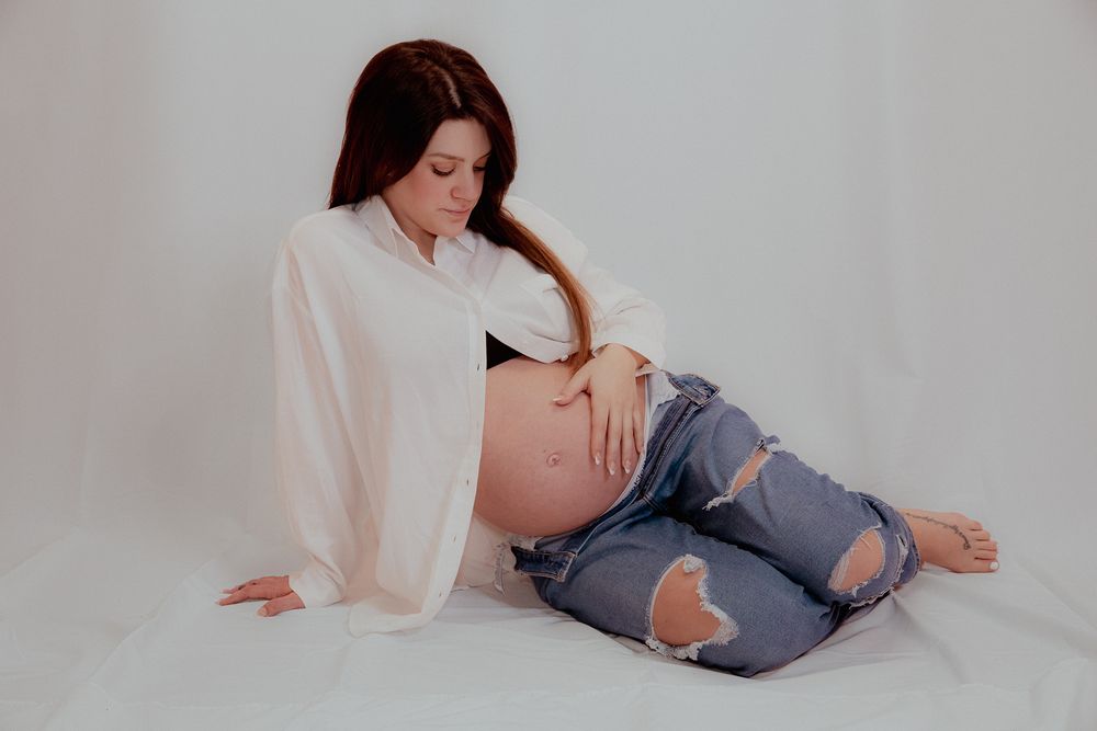Pregnant woman in white shirt and ripped jeans posing during maternity photoshoot.