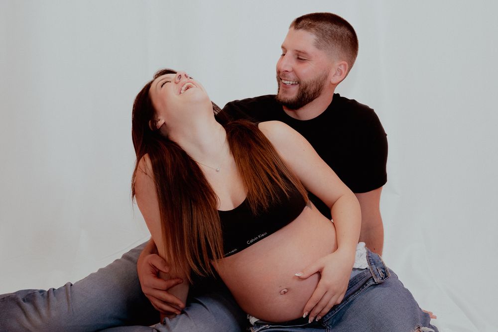 Expectant couple sharing joyful moment during maternity photoshoot against white background.