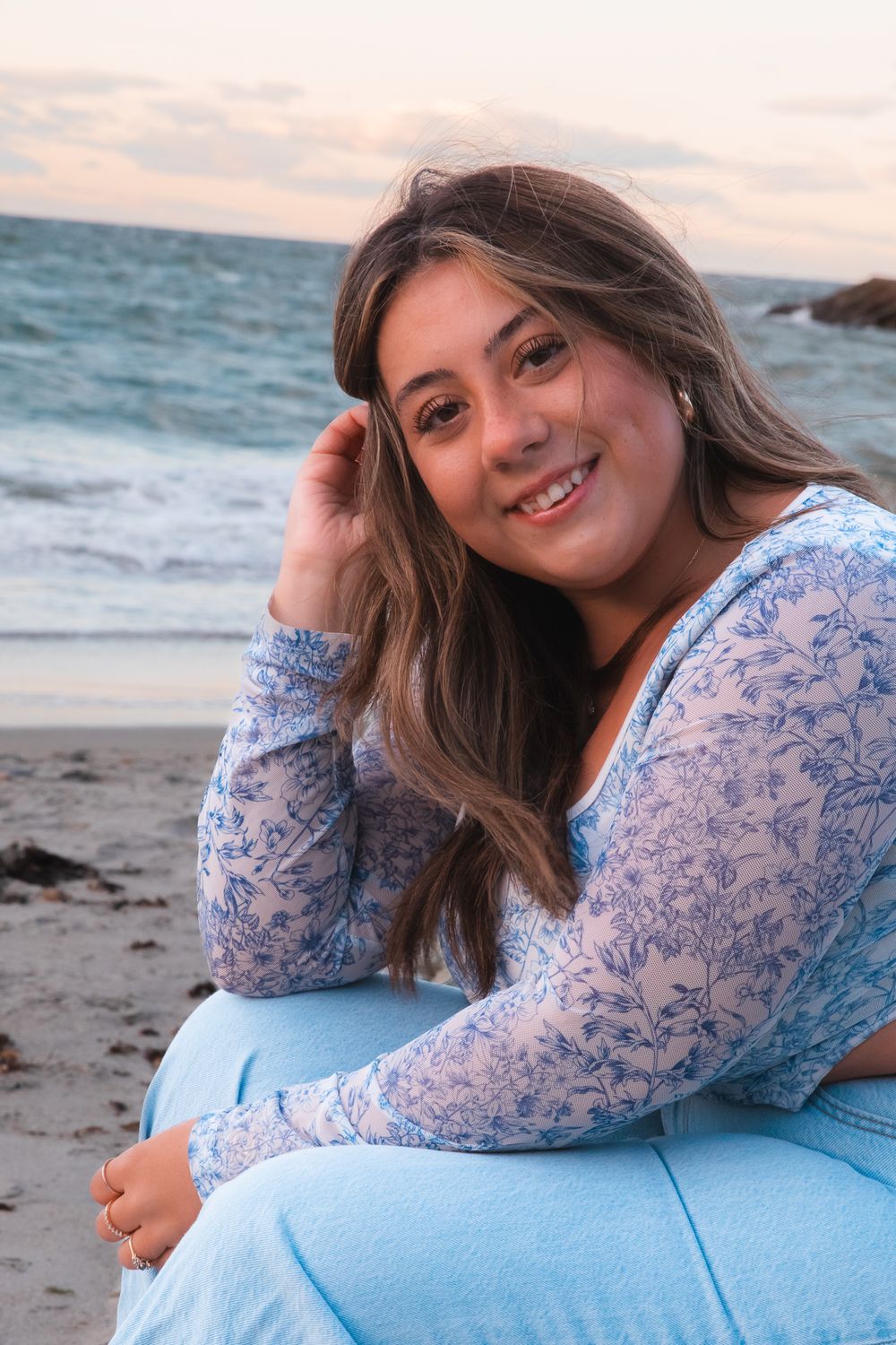 Portrait of woman in blue floral top sitting on beach at sunset.