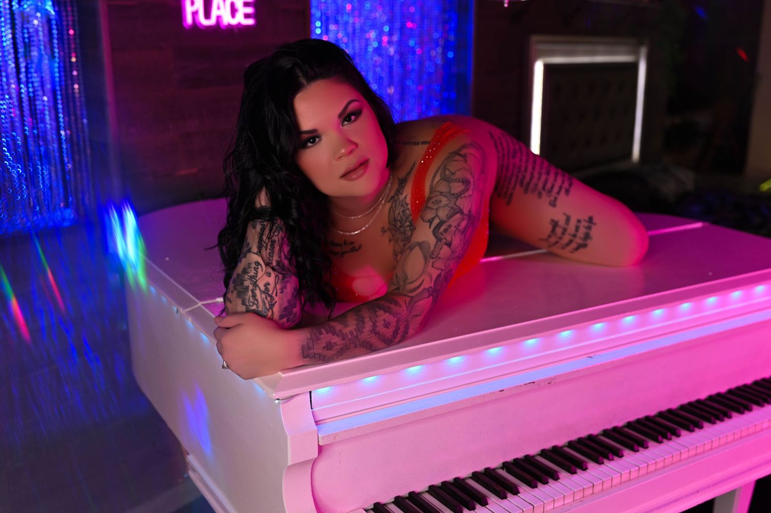Artistic boudoir photo with pink and blue lighting featuring a white piano.