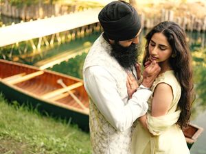 South Asian couple in traditional attire sharing a romantic moment near wooden canoes by a serene green waterway.