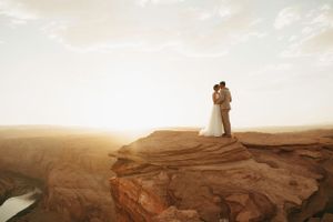 A silhouetted couple stands together on red rock formations at sunset.