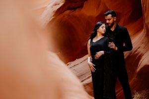 A romantic couple pose in black attire against smooth orange canyon walls.