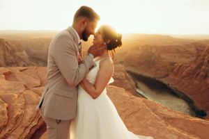 A couple shares an intimate moment on red cliffs overlooking a canyon at sunset.