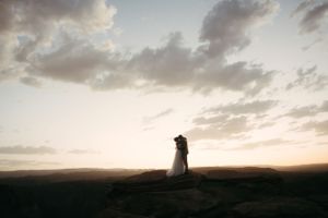 A couple stands with their horse in formal attire on desert salt flats at sunset.