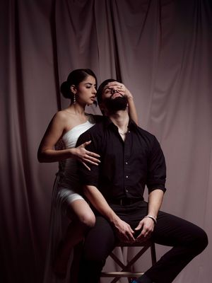 A couple in a romantic pose against a dark backdrop, with dramatic lighting creating an intimate atmosphere.