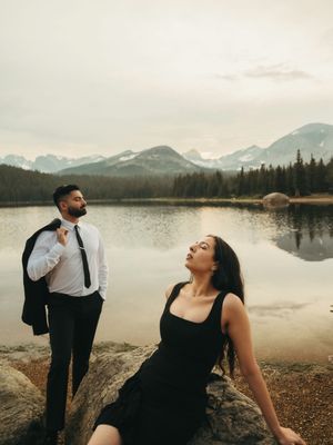 A couple shares joyful moments by a serene mountain lake during a romantic photoshoot at sunset.