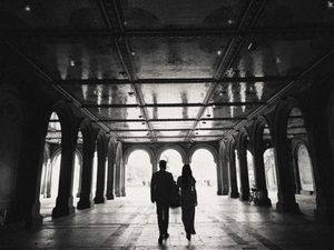 Silhouettes of people walking through a dark tunnel with dramatic lighting and architectural columns.