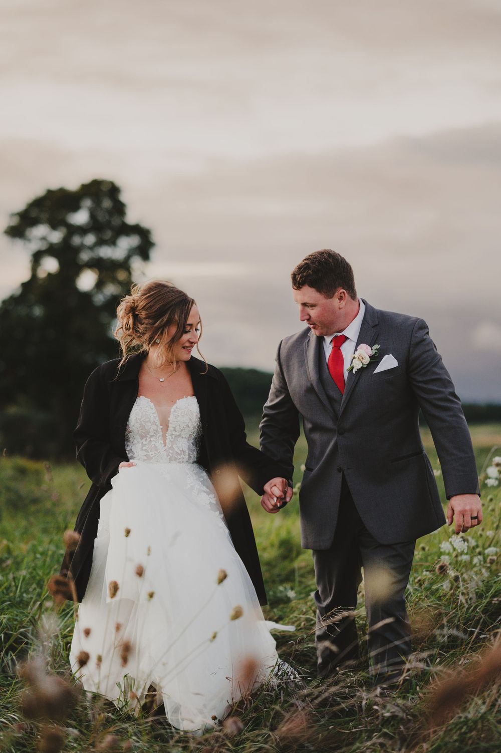 A couple walks hand in hand through a wildflower field during their wedding photoshoot.
