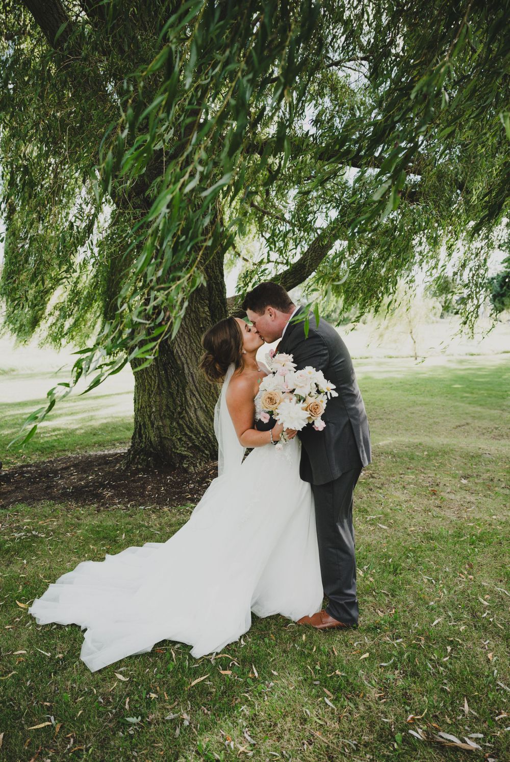 A couple shares their first kiss under a beautiful weeping willow tree on their wedding day.