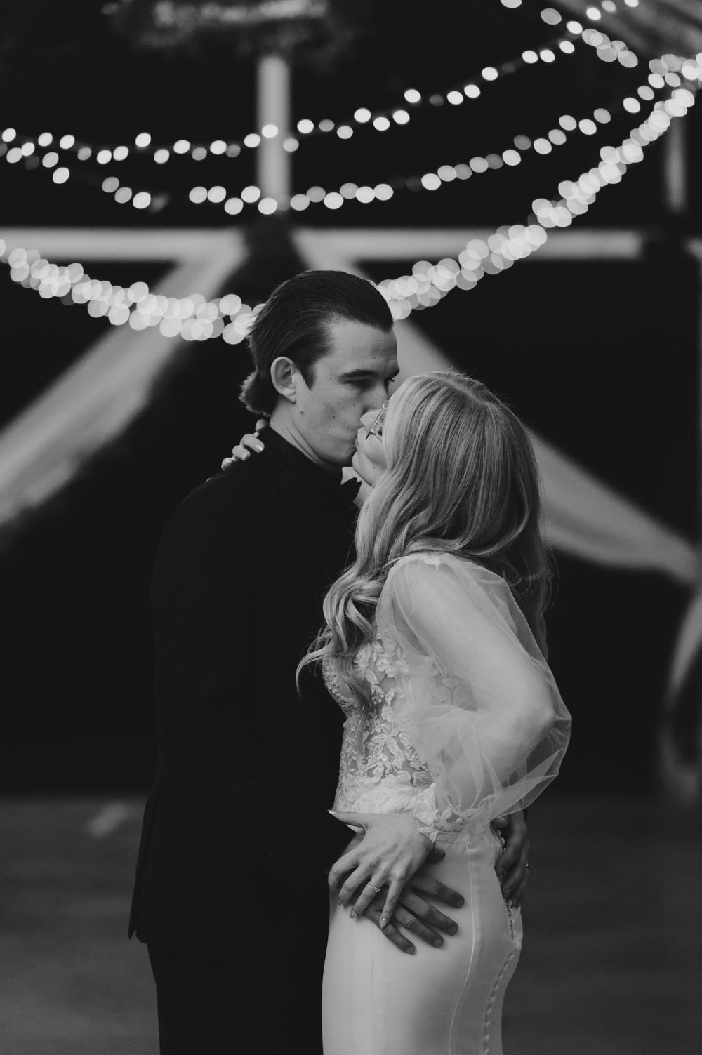 An intimate dance moment under twinkling lights at an evening wedding reception.