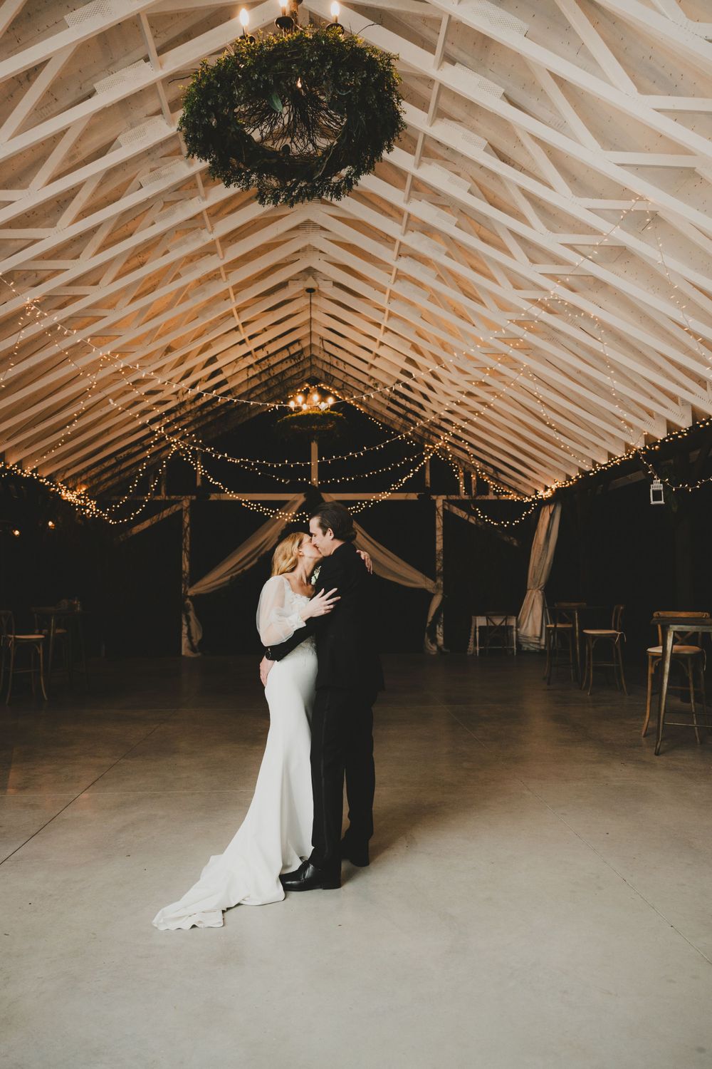 A romantic first dance in a rustic barn venue with twinkling lights and exposed wooden beams.