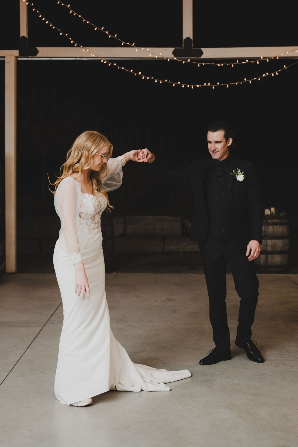 A couple shares a playful dance moment under string lights at their wedding reception.