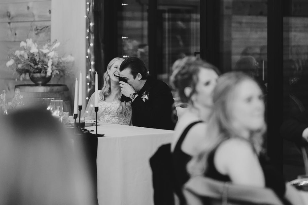 A black and white reception photo capturing intimate moments between guests at the dinner table.