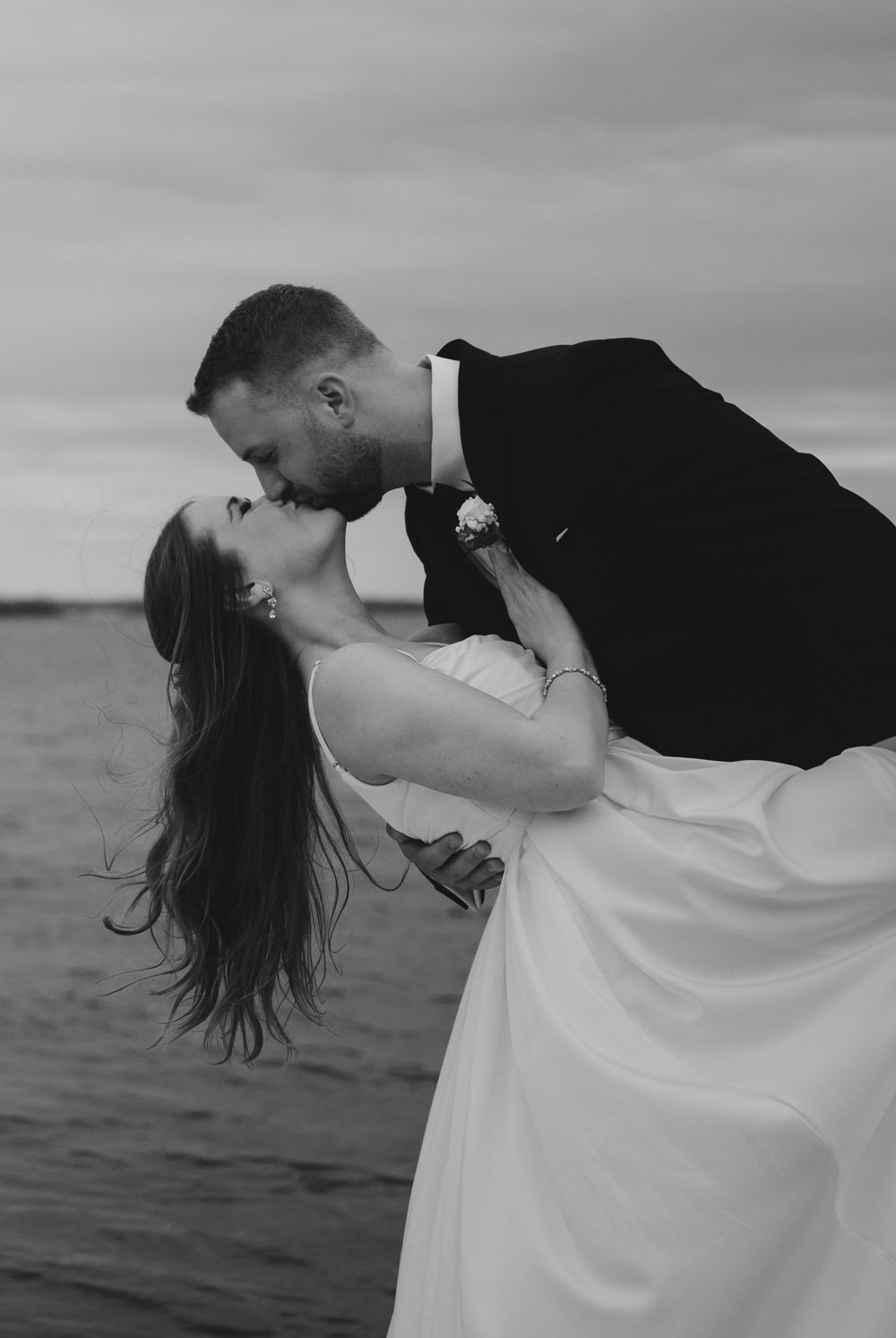 Dramatic black and white dip kiss by waterfront.