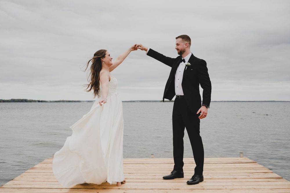 Couple dancing on wooden pier overlooking calm water.