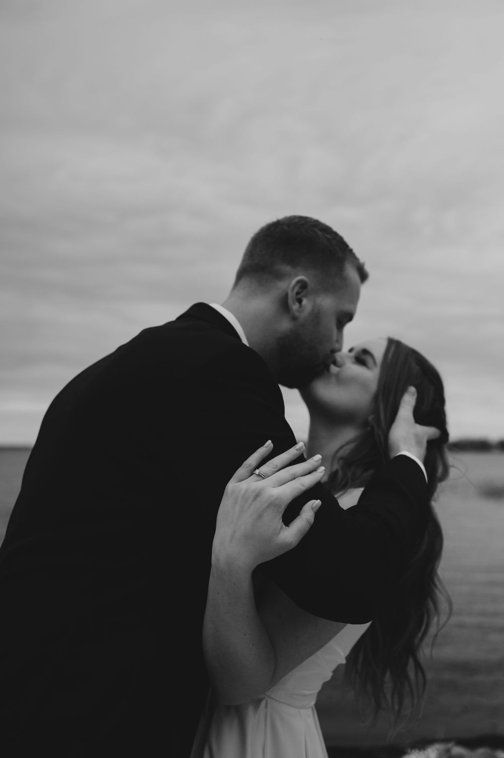 A romantic black and white portrait of a couple sharing an intimate kiss against a moody sky.
