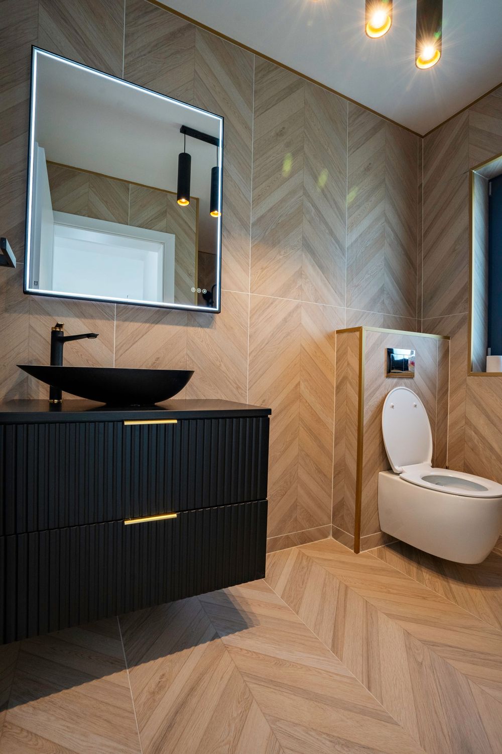 Modern bathroom interior with black vanity, vessel sink, and chevron pattern tile walls.