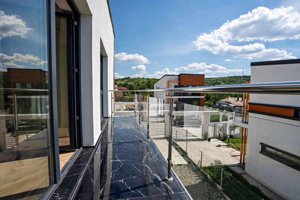 Modern apartment balcony with glass railings and marble flooring overlooking residential area.