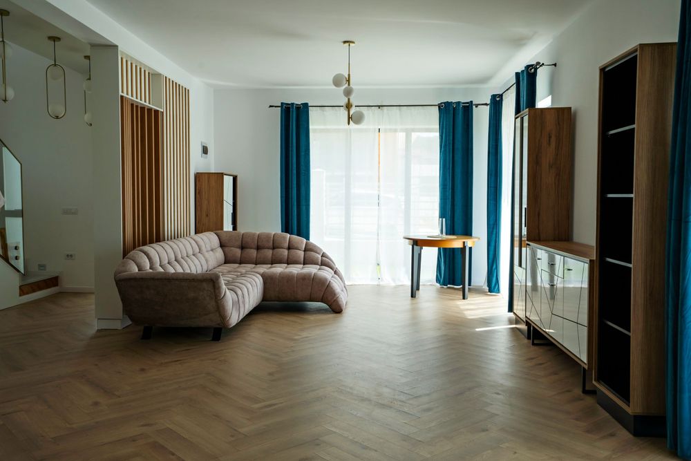 Spacious living room with beige curved sofa, herringbone floors, and blue curtains.