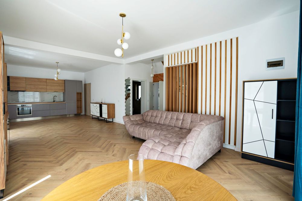Open concept living space with curved sofa, wooden room divider, and modern kitchen.