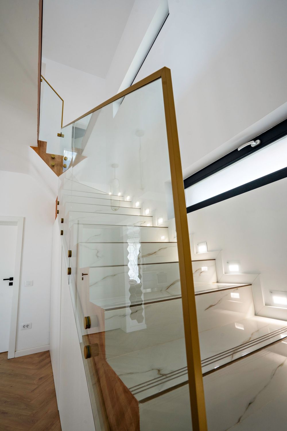 Contemporary stairwell featuring white walls, wooden accents, and sleek glass balustrades bathed in natural light.