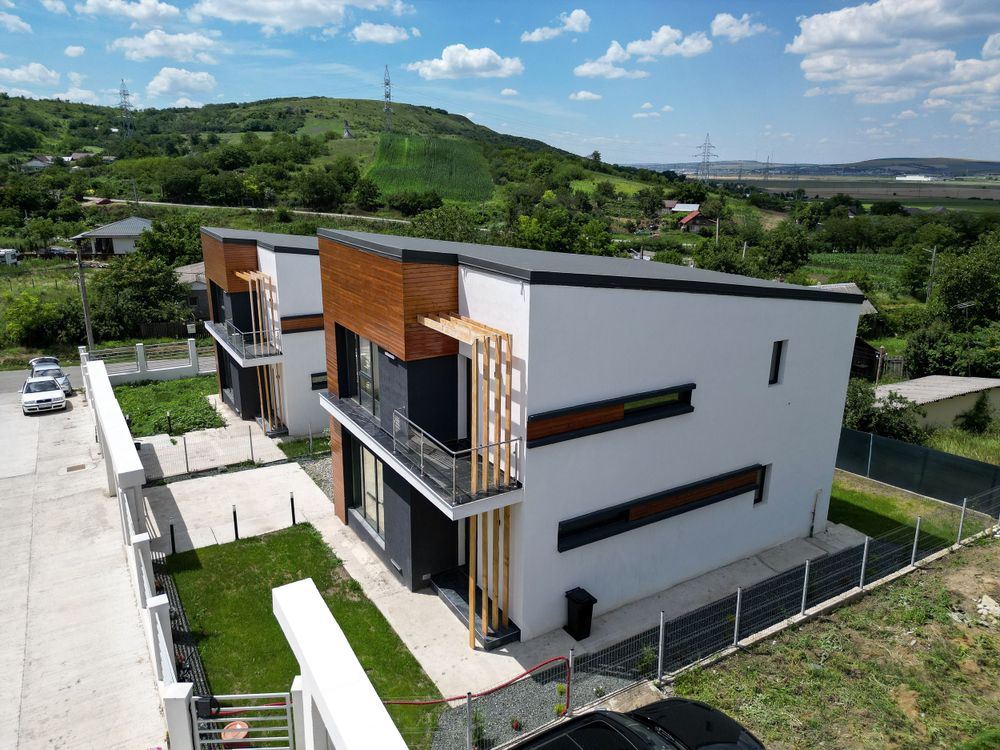 Modern commercial building with white and wood exterior set against green rolling hills on a sunny day.