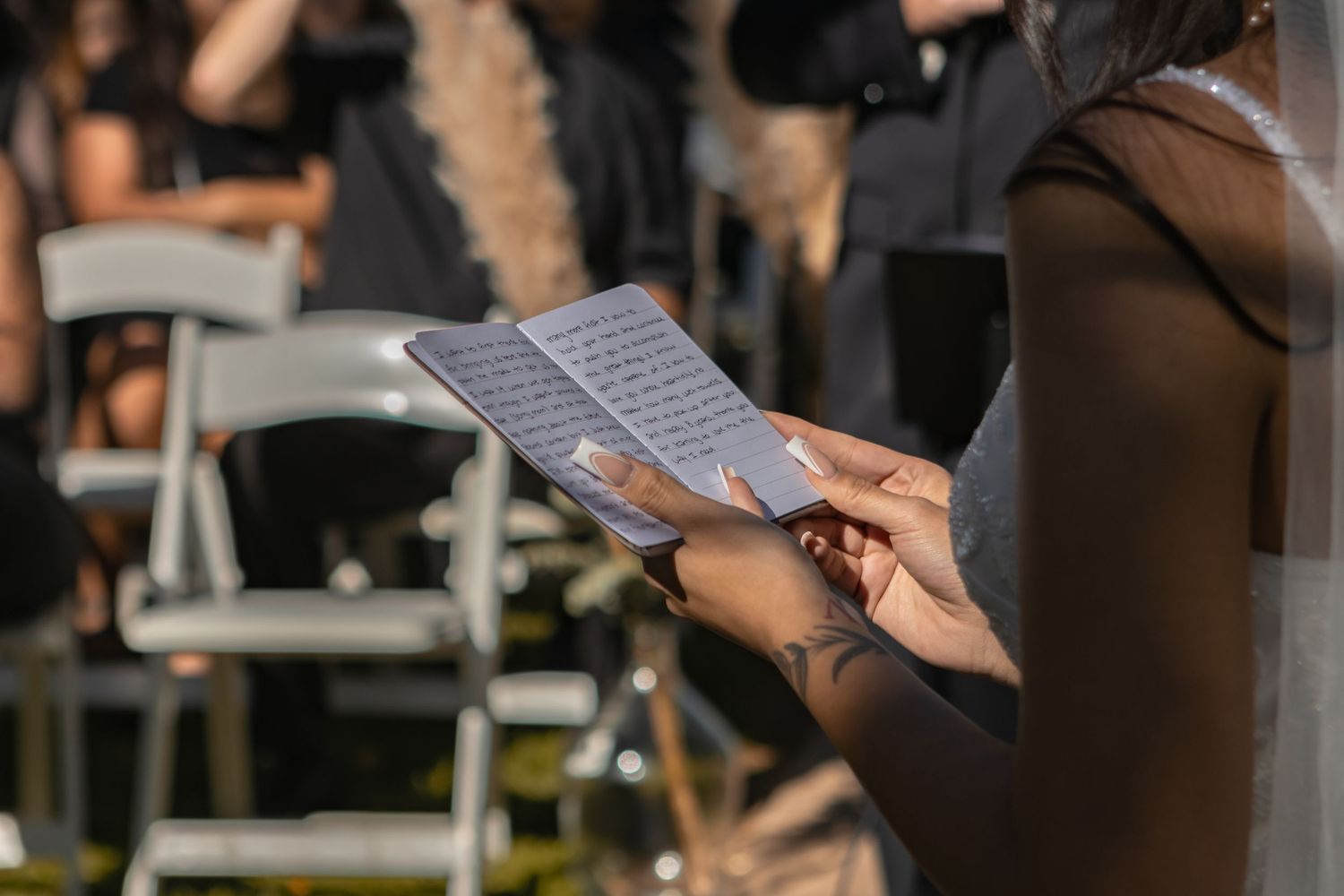 A bride reads her vows at the altar. She has a few visible tattoos, some black, some red, and a spaghetti strap wedding dress with sparkles