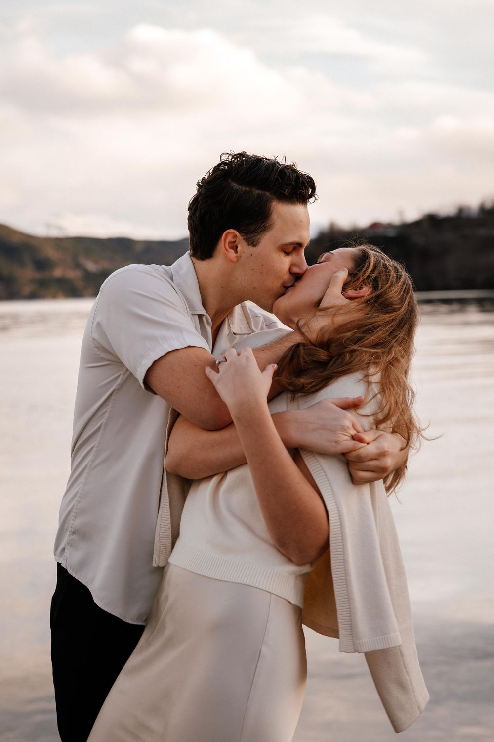 A romantic couple sharing a passionate kiss at sunset by the water's edge in a dreamy beach setting.