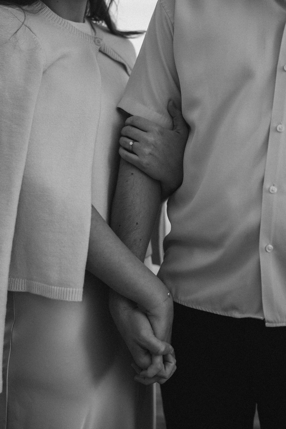 Black and white photo showing intimate embrace and holding hands while wearing light colored clothing.