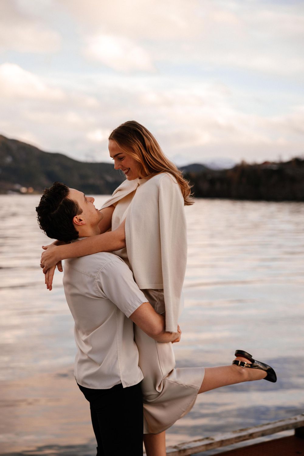 Romantic couple embraces by the lake at sunset with mountains in background, creating an intimate silhouette.