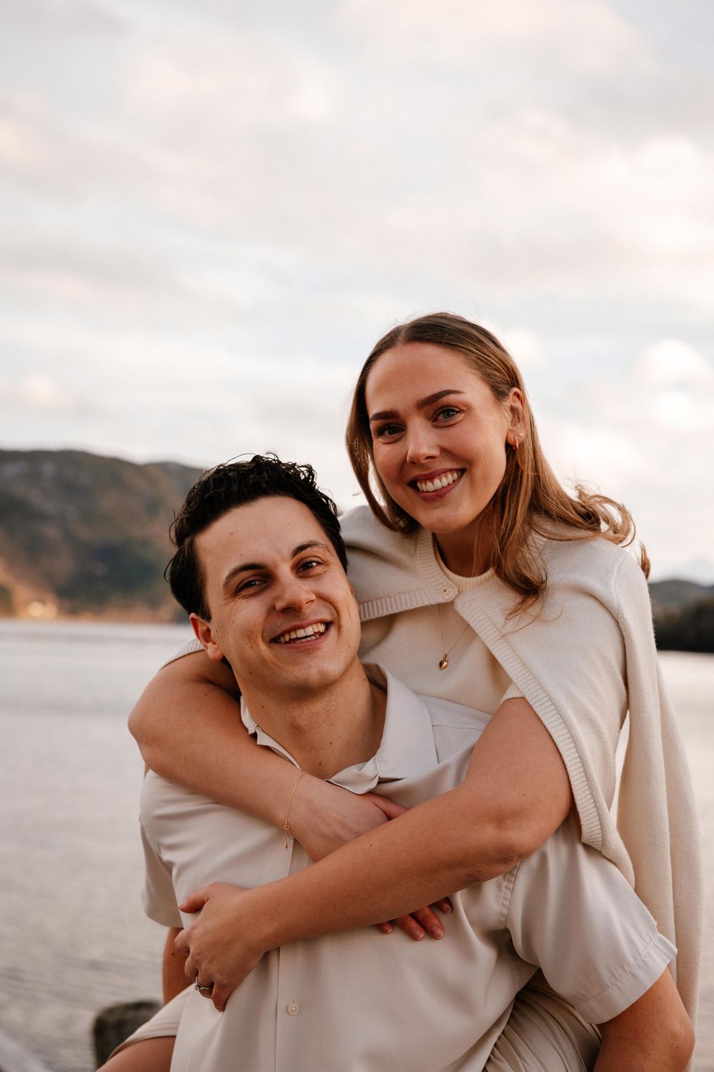 A happy couple embraces on a beach during golden hour with mountains visible in the background.