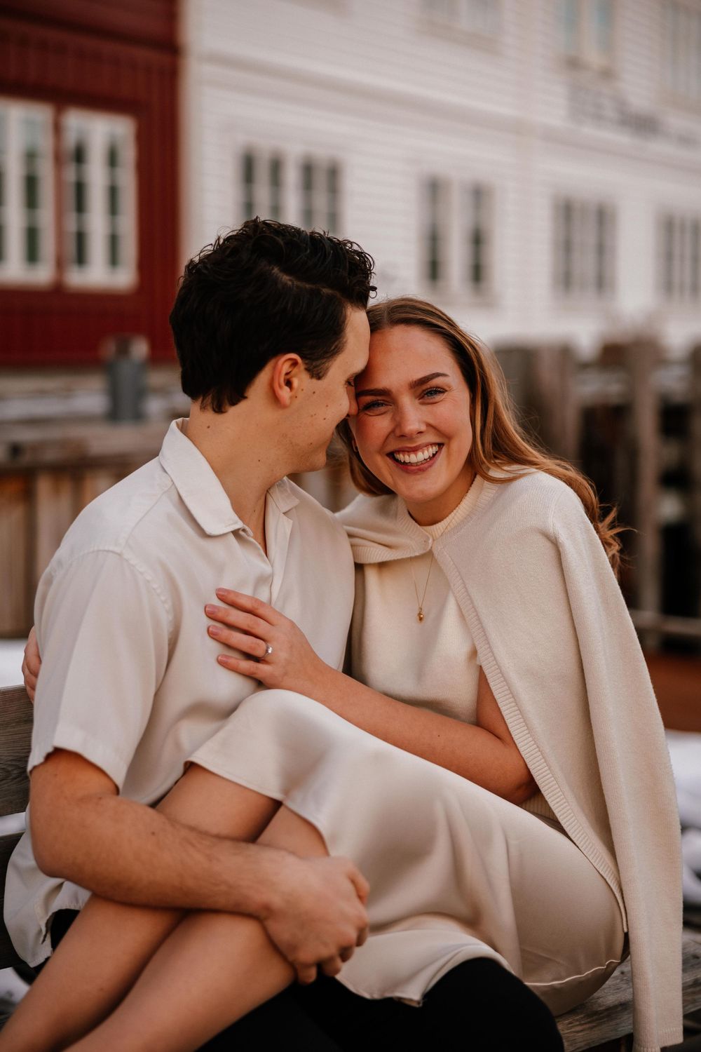 A joyful intimate moment shared between a couple wearing light colored clothing against a rustic building backdrop.