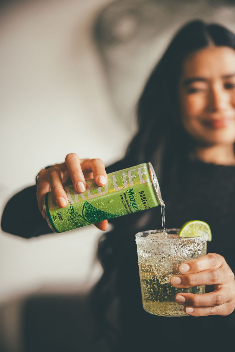 Woman pouring a lime-flavored LOCA LIFE canned drink into an ice-filled glass garnished with a lime slice.