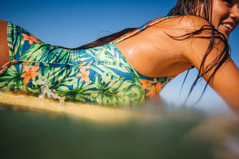 Woman in tropical print bikini lying on surfboard in ocean waves on a sunny day.
