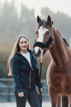 Person in black jacket bonding with a friendly brown horse in a paddock.