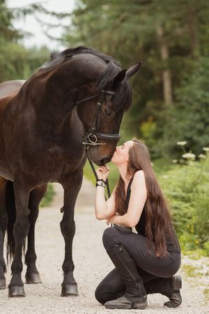 A special bonding moment between a dark horse and rider on a forest path.