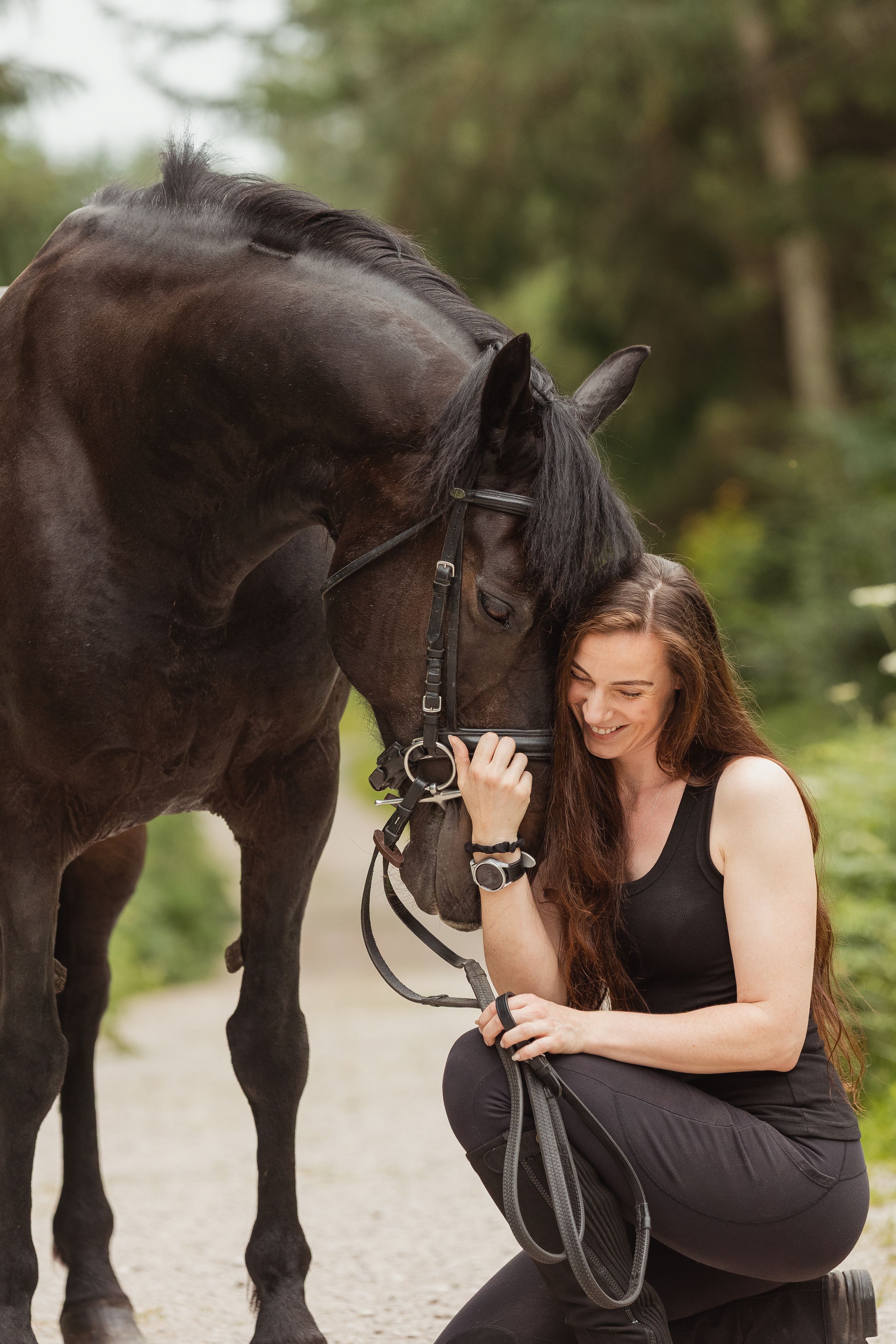 An intimate portrait of a dark horse and rider sharing a moment on a forest path.