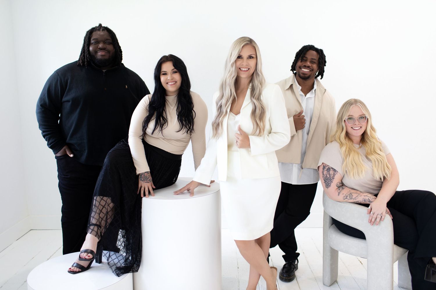 A diverse group of people posing together in white outfits against a white studio backdrop.