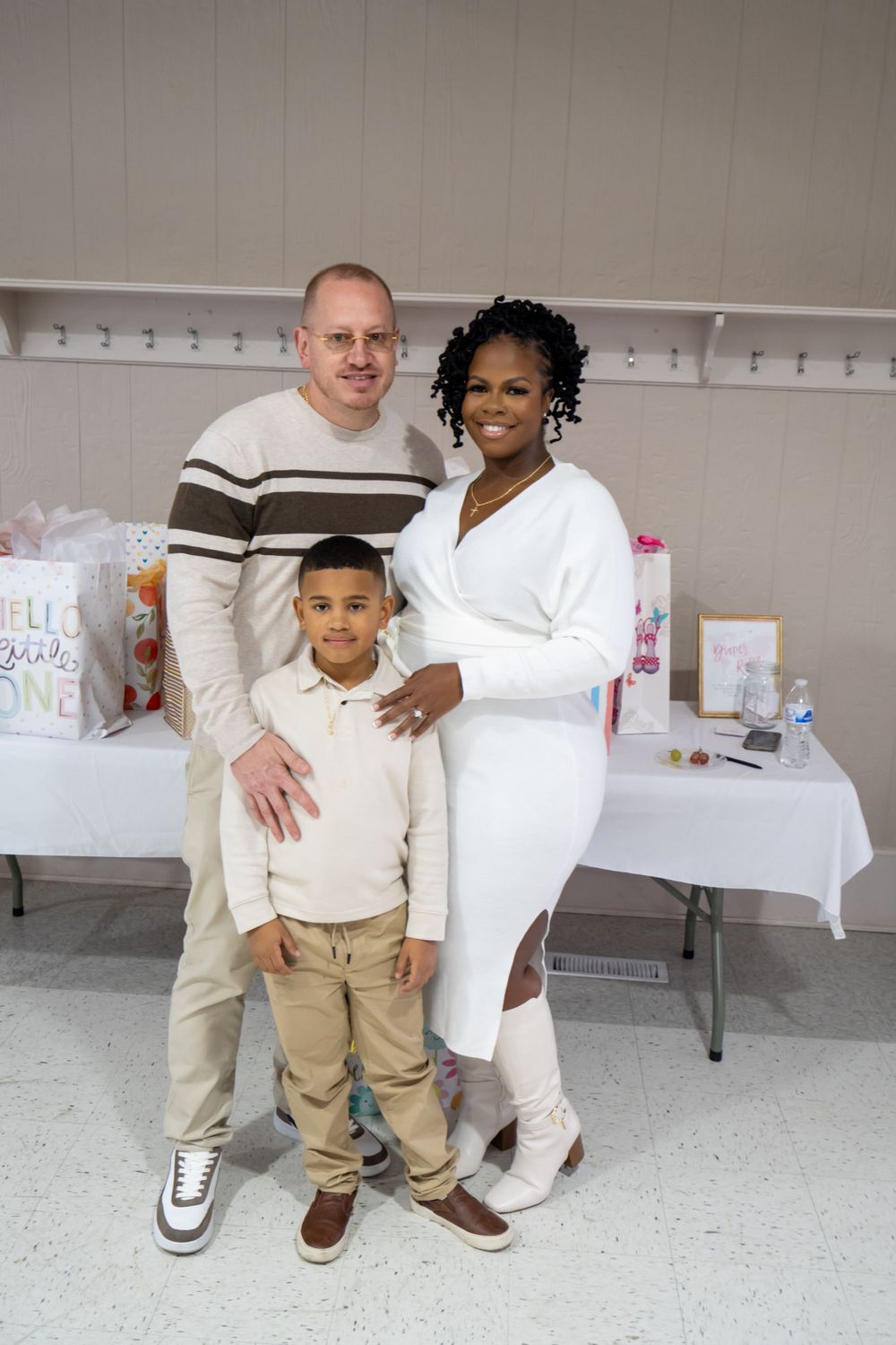 Family poses together at a celebration with wrapped gifts and decorations on a table in the background.