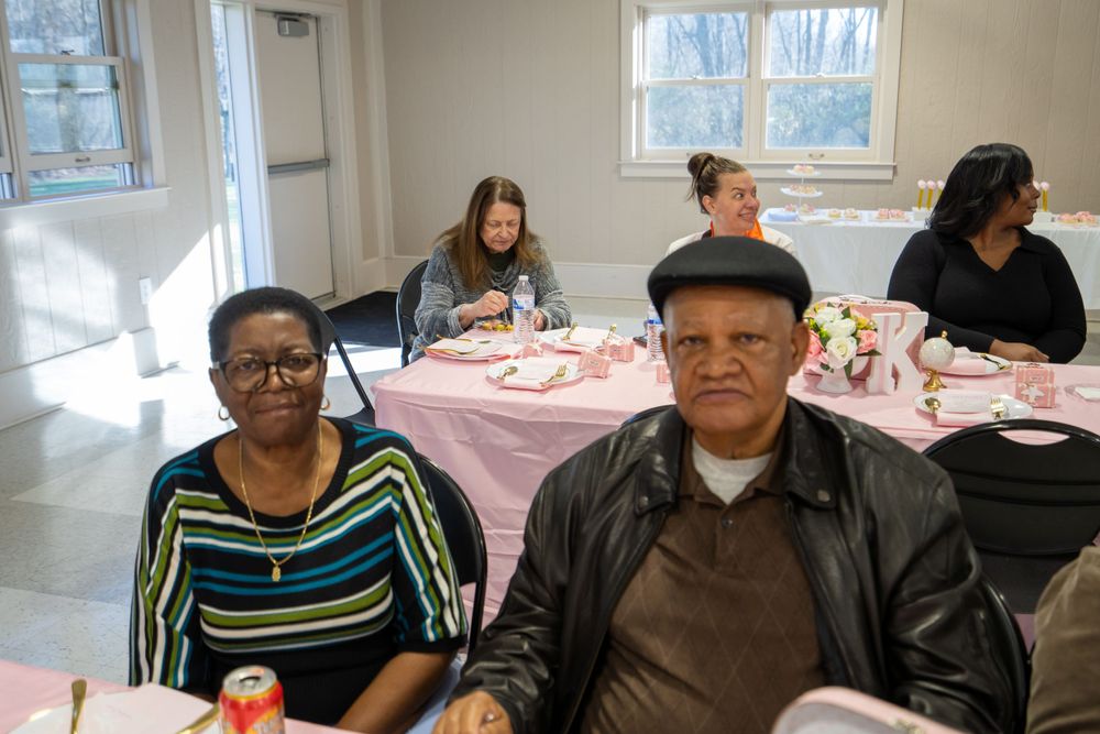 Community members gathered at a round pink-clothed table for a social event in a bright room.