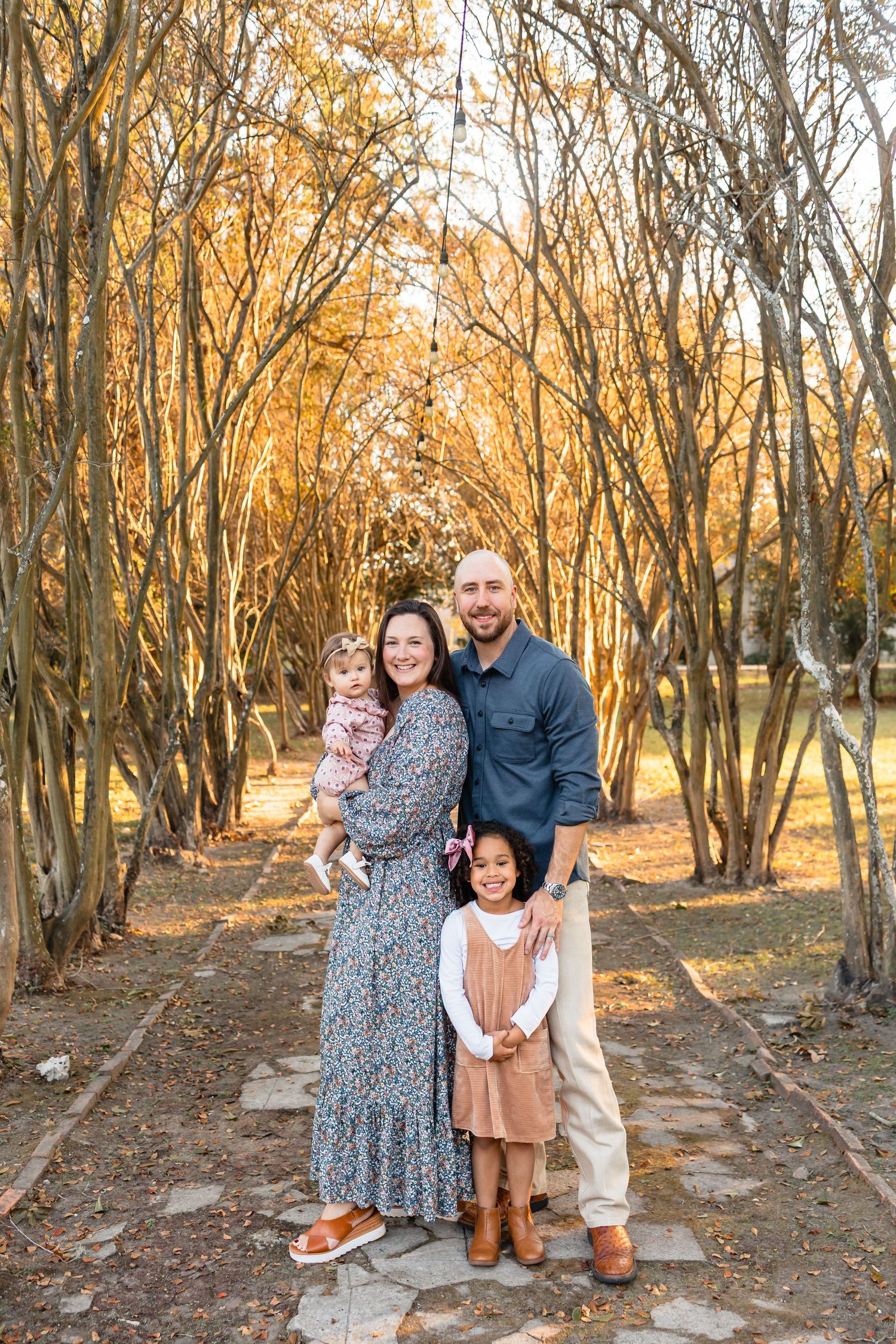 Happy family of four posing together on a stone path surrounded by golden autumn trees.