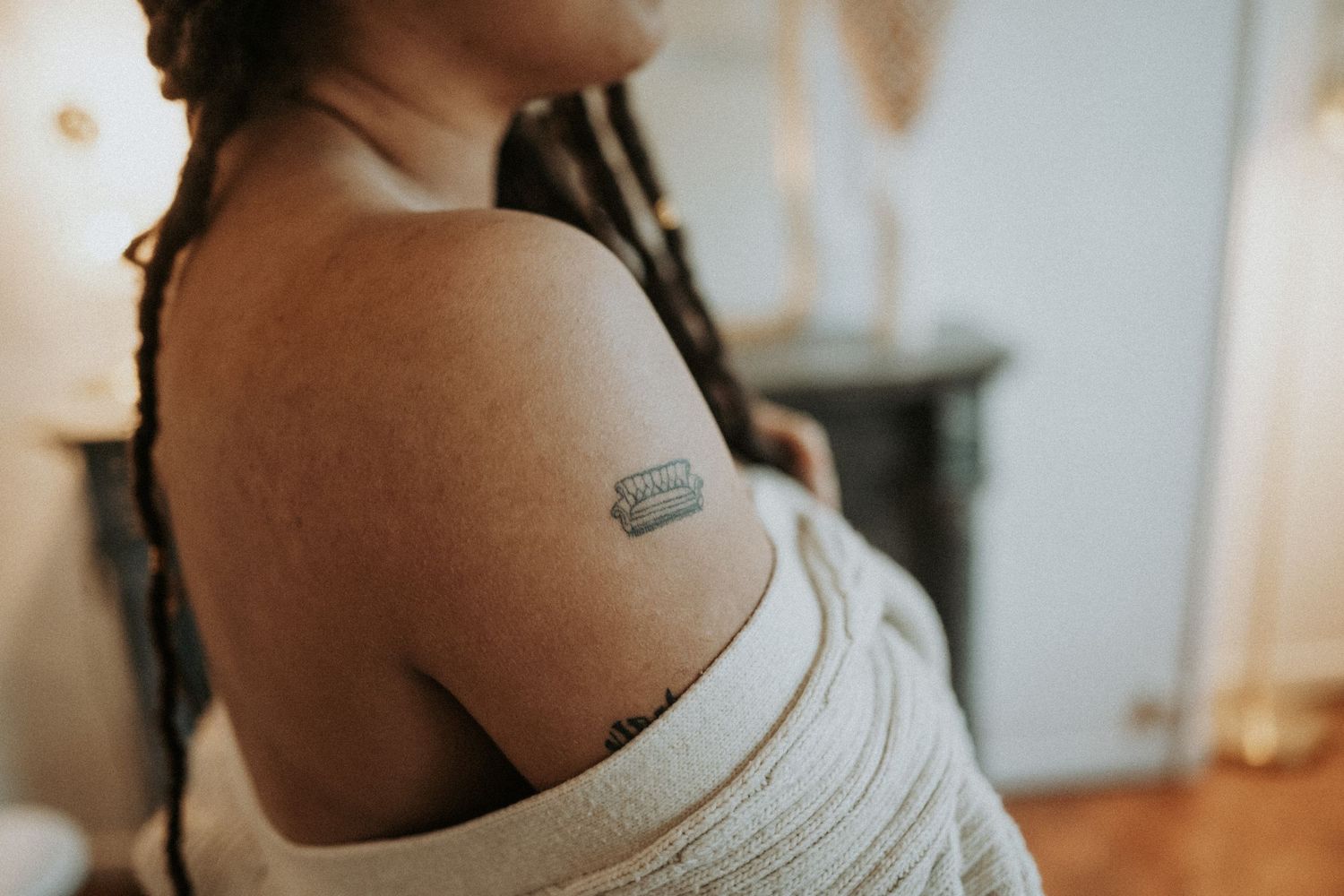 Close-up detail of shoulder with tattoo and white off-shoulder sweater.